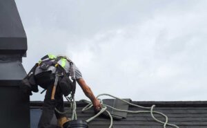 A residential roofer inspecting shingles and flashing on a pitched suburban home roof.