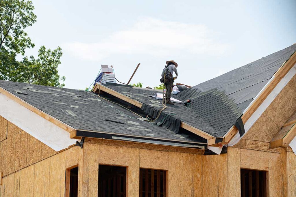 Homeowner comparing roof shingle samples beside a house with siding, trim, and brick.