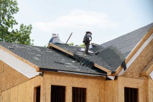 Homeowner comparing roof shingle samples beside a house with siding, trim, and brick.